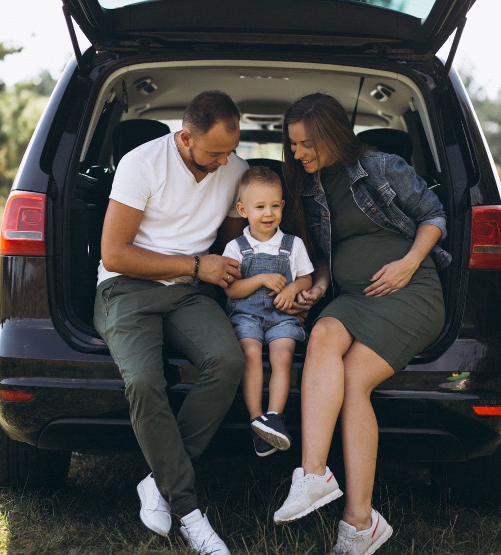 A happy family sitting in the open trunk of their SUV, enjoying a moment together outdoors.