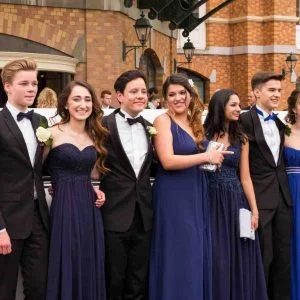 Group of elegantly dressed young adults posing for a prom night outside a luxury venue.